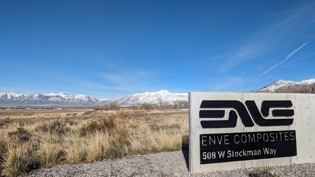 The ENVE Composites sign beside an open field with the snow-covered Wasatch mountains behind it.